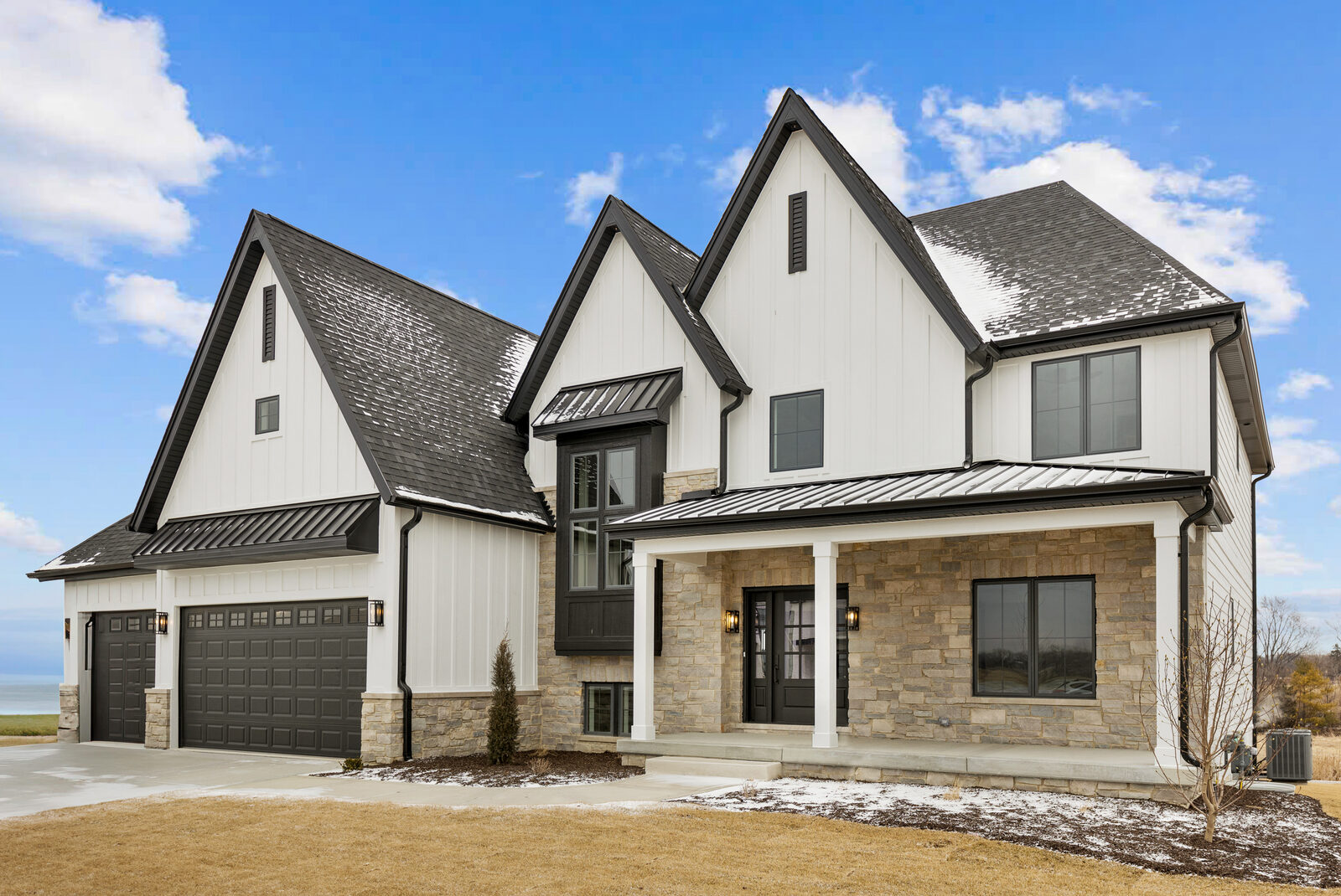 Modern farmhouse custom home with white board-and-batten siding, black roofline and windows, and layered front gables built by Spyglass