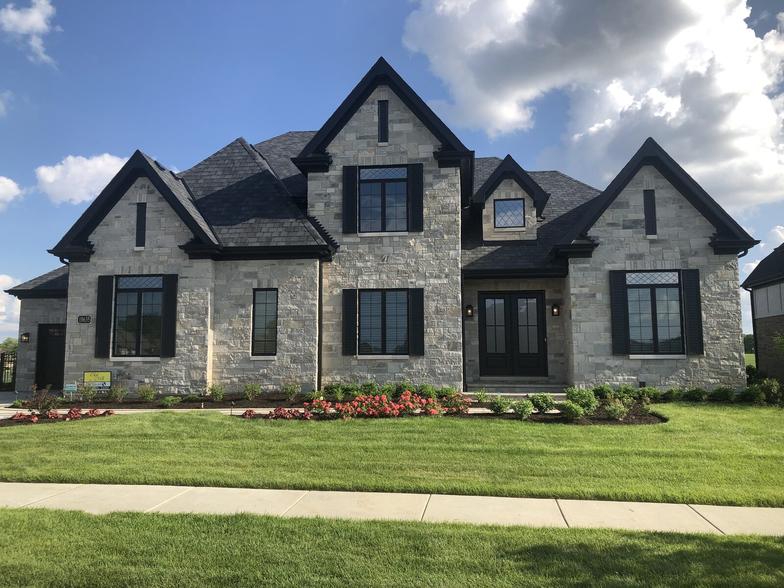 All-stone Tudor custom home with black shutters, double door entry and layered front gables built by Spyglass