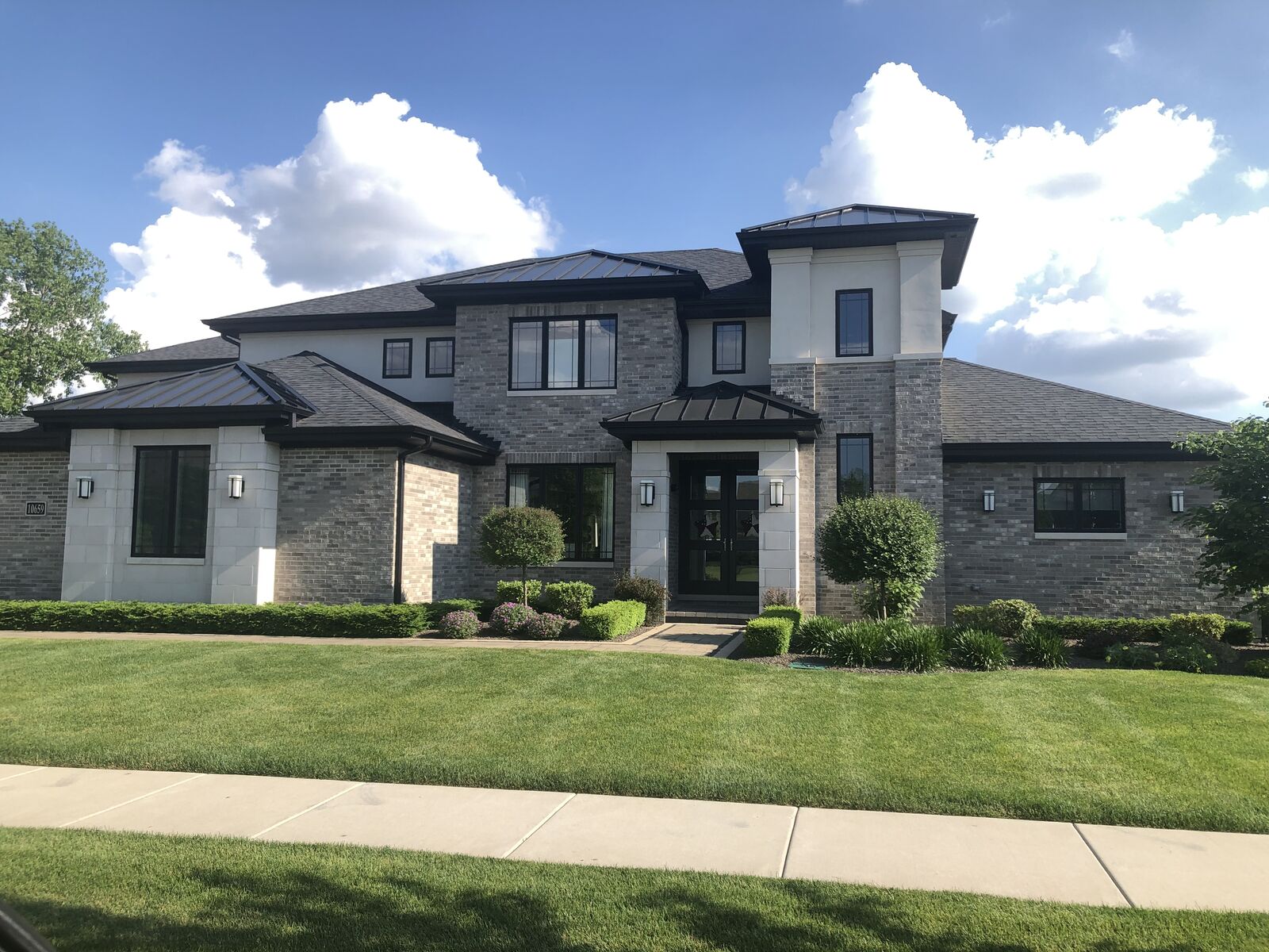 Modern prairie style custom home with gray brick, standing-seam metal roof accents and limestone by Spyglass