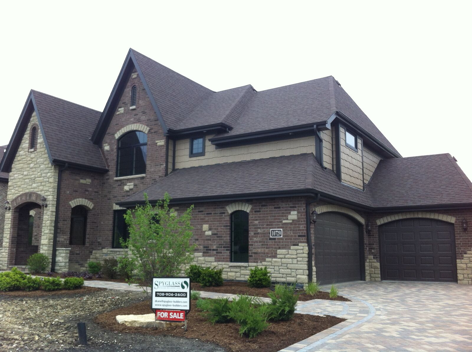 European style brick and stone custom home with arched garage doors and paver driveway built by Spyglass